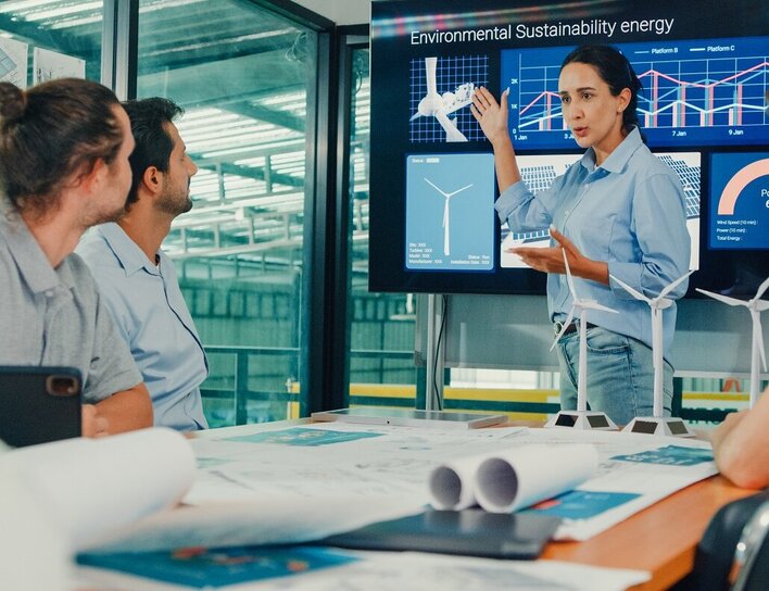 Bachelor Verfahrenstechnik Spezialisierung Energietechnologien Eine Ingenieurin präsentiert einem Team nachhaltige Energiekonzepte mit Windkraftmodellen und Datenvisualisierungen.