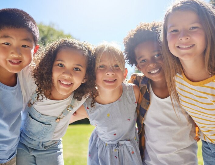 Gruppe fröhlicher Kinder im Sonnenschein Lächelnde Kinder stehen Arm in Arm im Freien bei strahlendem Sonnenschein.