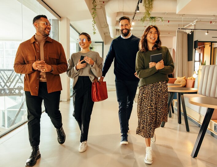 Vier junge Erwachsene im Gespräch beim Gehen durch ein modernes Büro.