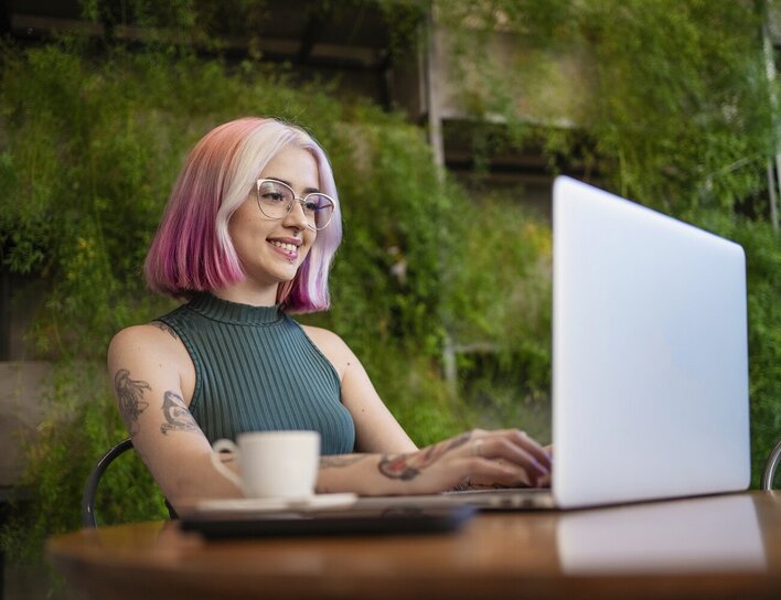 Eine junge Frau sitzt am Laptop vor einer grün bepflanzten Wand