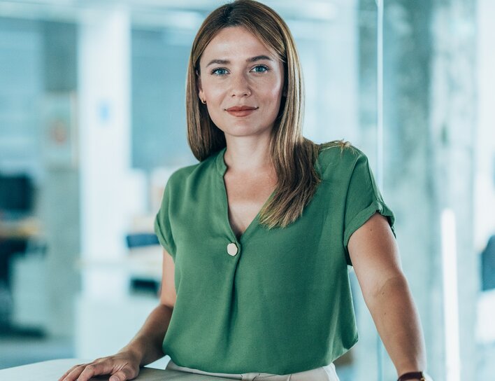 Eine Frau in einem modernen Büro schaut mit selbstbewusstem Blick in die Kamera.