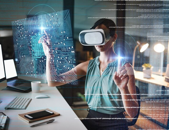 Spezialisierung Künstliche Intelligenz Frau mit Virtual-Reality-Brille sitzt an einem Schreibtisch und interagiert mit virtueller Benutzeroberfläche; futuristische Grafiken und ein digitaler Schaltkreis sind eingeblendet.