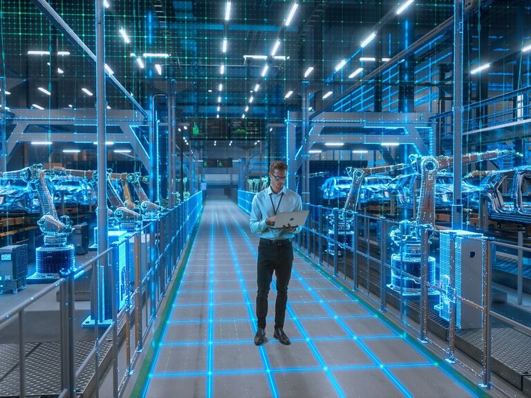 Ein Ingenieur mit Laptop geht durch eine digital visualisierte Smart Factory mit vernetzten Robotern und automatisierter Fahrzeugproduktion.