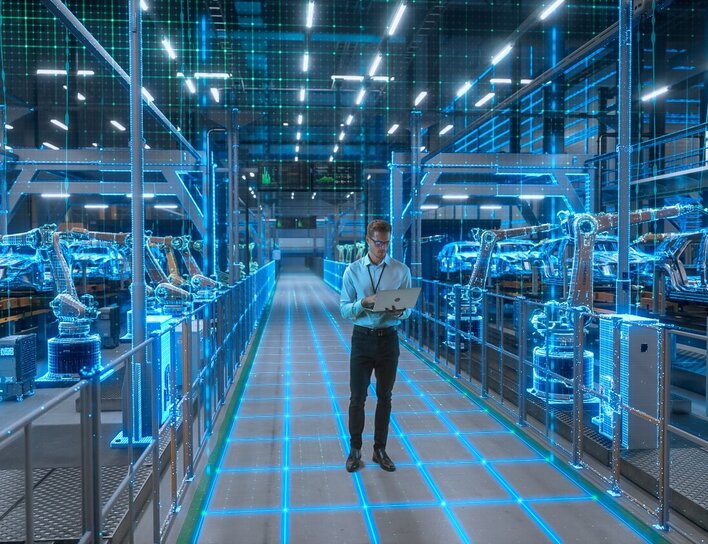 Ein Ingenieur mit Laptop geht durch eine digital visualisierte Smart Factory mit vernetzten Robotern und automatisierter Fahrzeugproduktion.