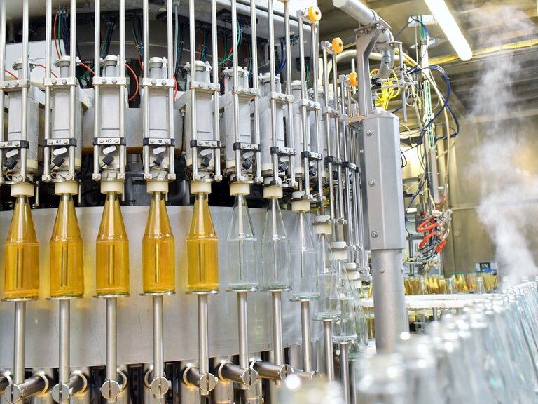 Eine automatisierte Abfüllanlage befüllt Glasflaschen mit einem gelblichen Getränk in einer modernen Produktionslinie.