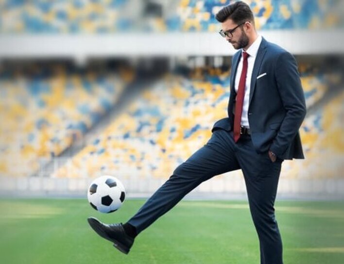 Mann im Business-Anzug jongliert Fußball auf Stadionrasen Mann im Business-Anzug jongliert Fußball auf Stadionrasen