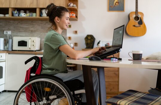 Frau im Rollstuhl arbeitet an einem Laptop in ihrer Küche