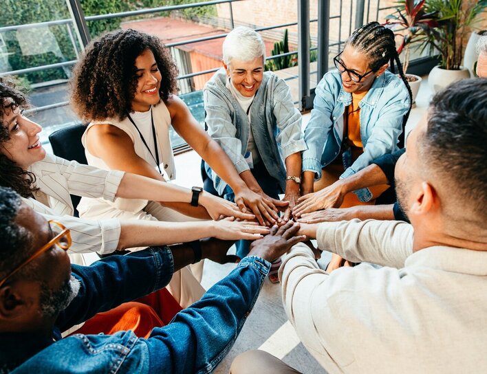Diverse Gruppe erwachsener Menschen hält ihre Hände in der Mitte zusammen.