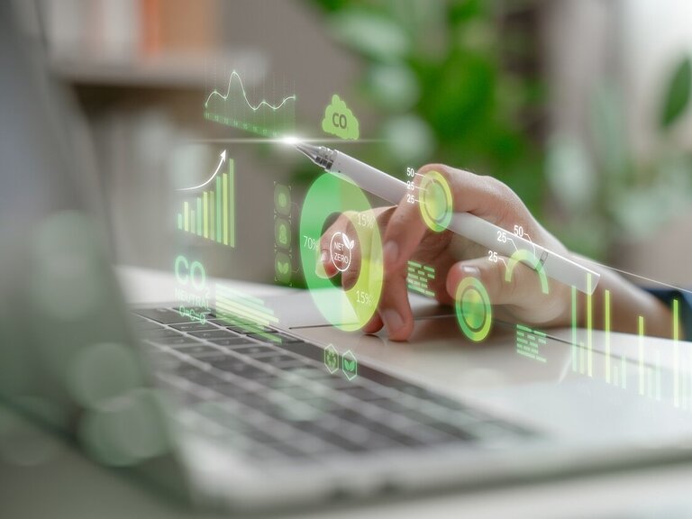 Eine Hand bedient mit einem Stift ein digitales Dashboard mit Nachhaltigkeits- und CO₂-Daten auf einem Laptop.