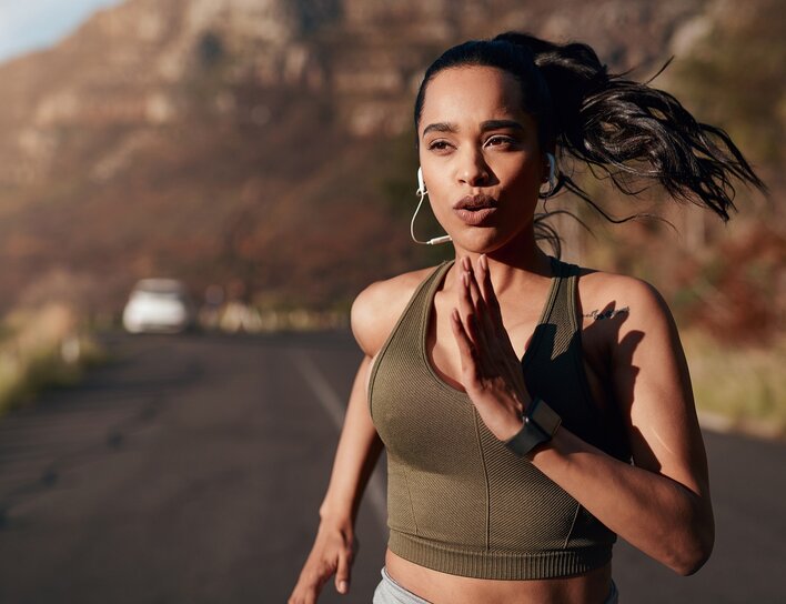 Frau joggt auf einer Landstraße vor einer bergigen Kulisse, bei Tageslicht.